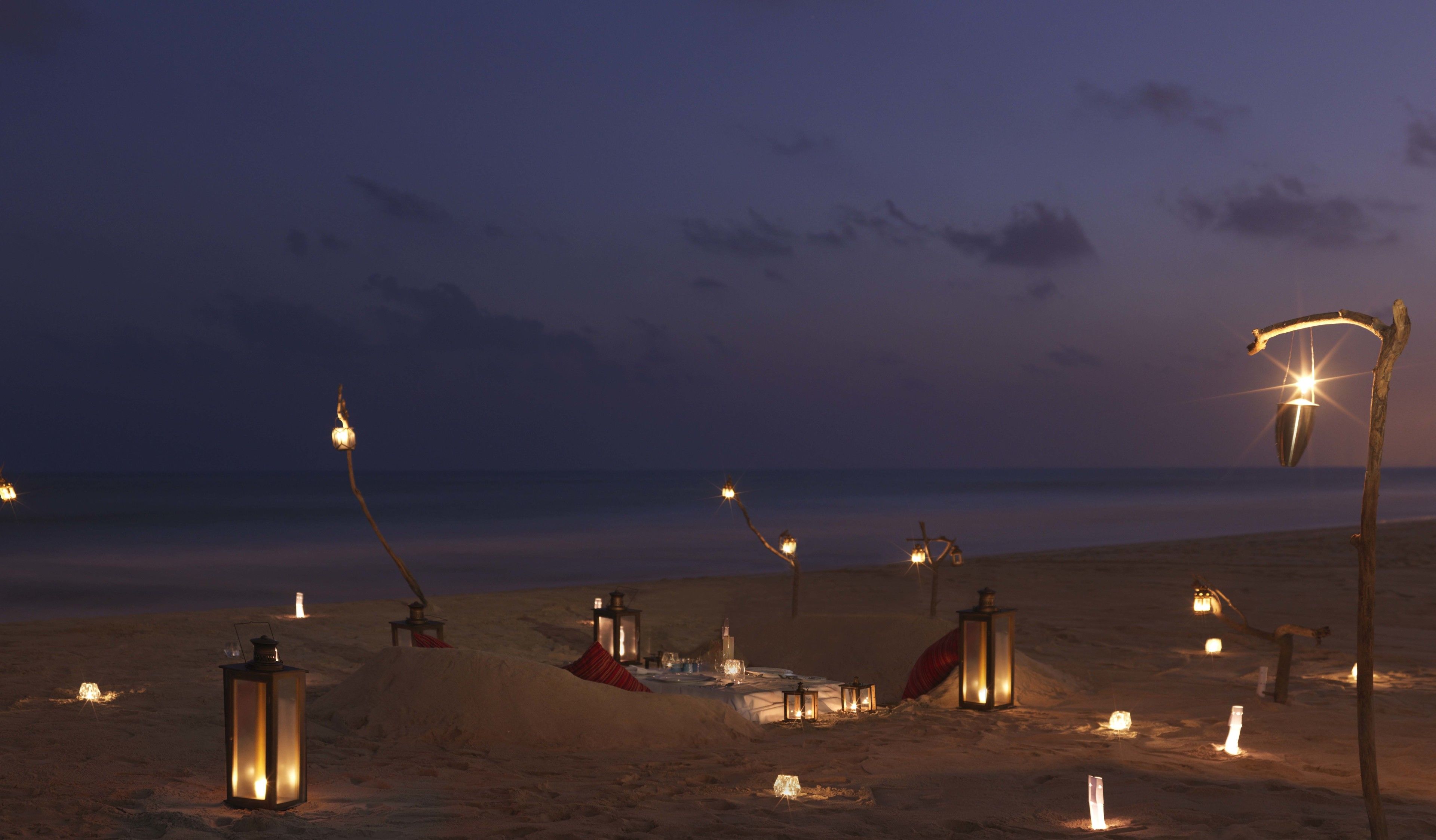 A desert scene with multiple lanterns and a small structure on the sand.