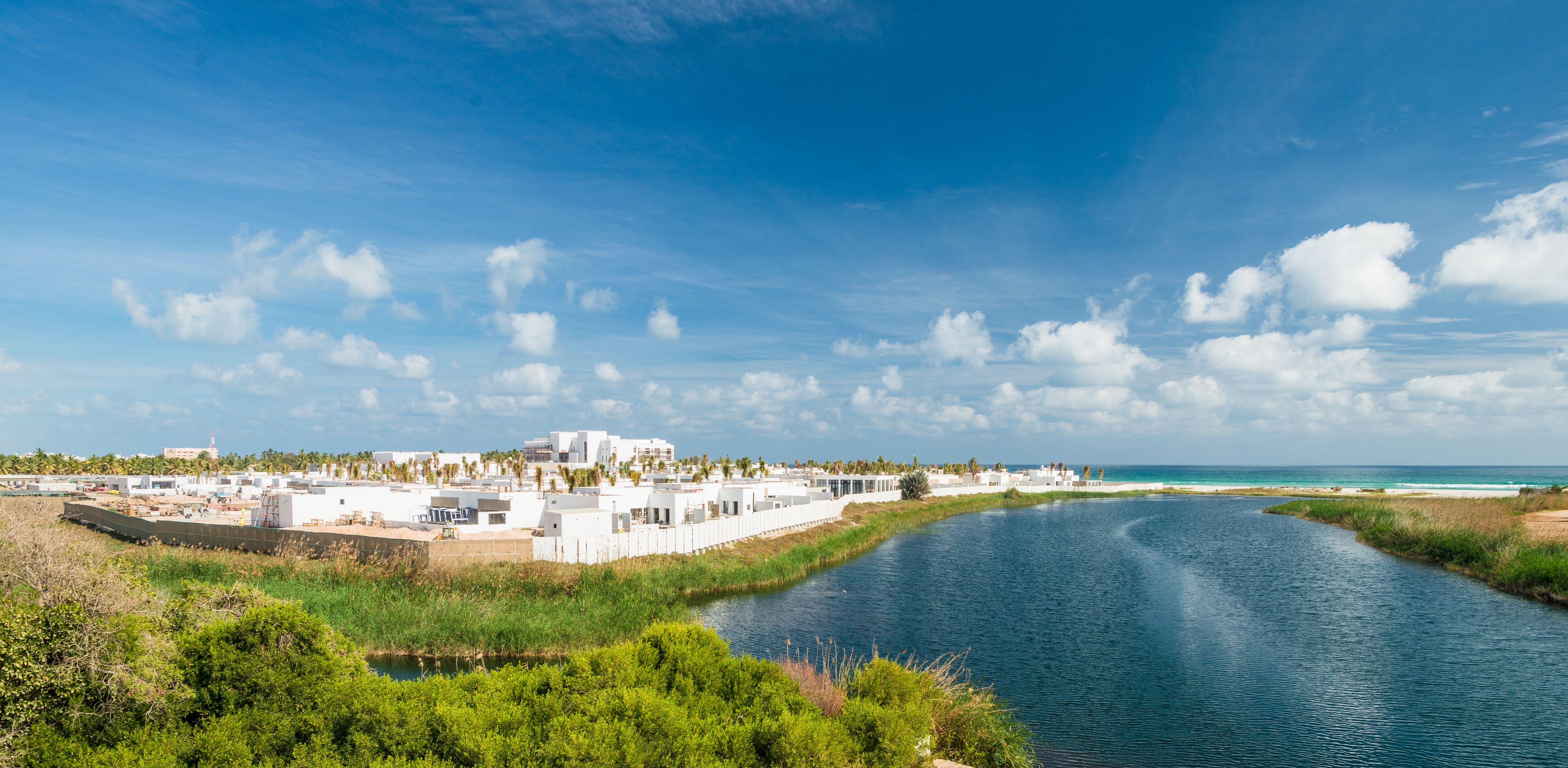 A coastal resort with white buildings, a river, and a beach.