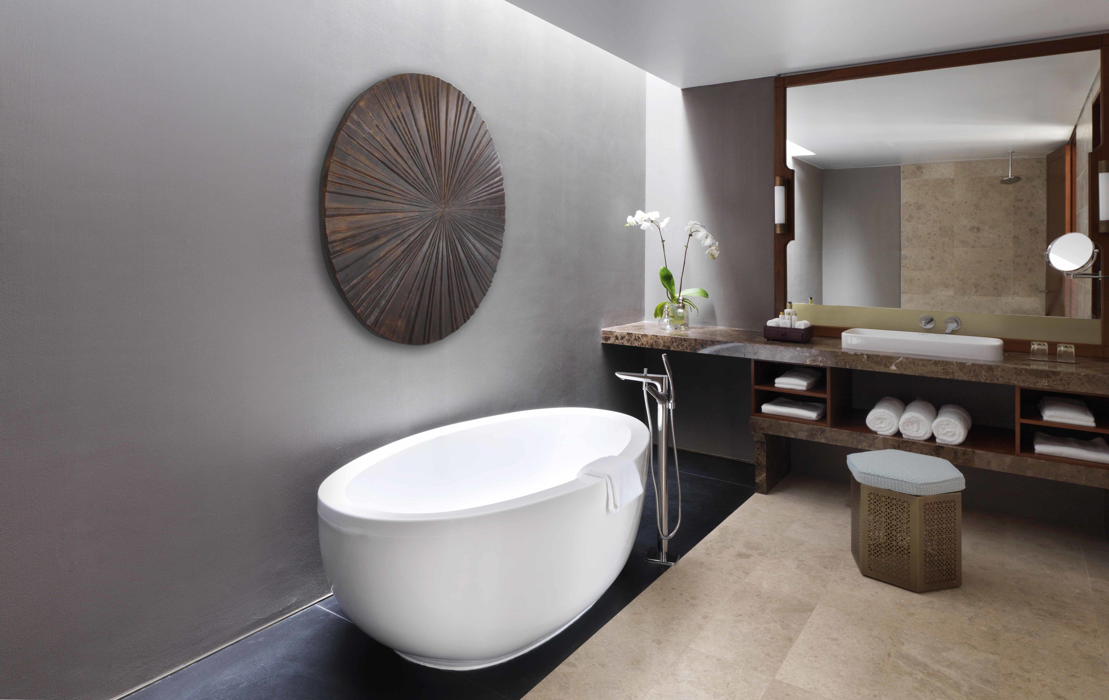 A modern bathroom with a freestanding bathtub, a large mirror, and a decorative wall piece.