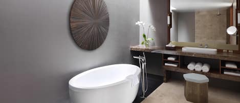 A modern bathroom with a freestanding bathtub, a large mirror, and a decorative wall piece.