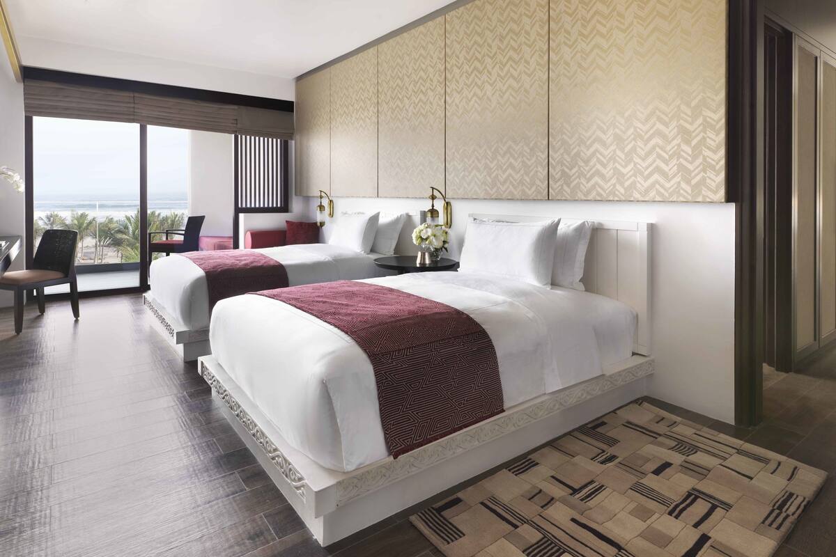 A hotel room with two beds, a large window with a view, a desk, and a chair.