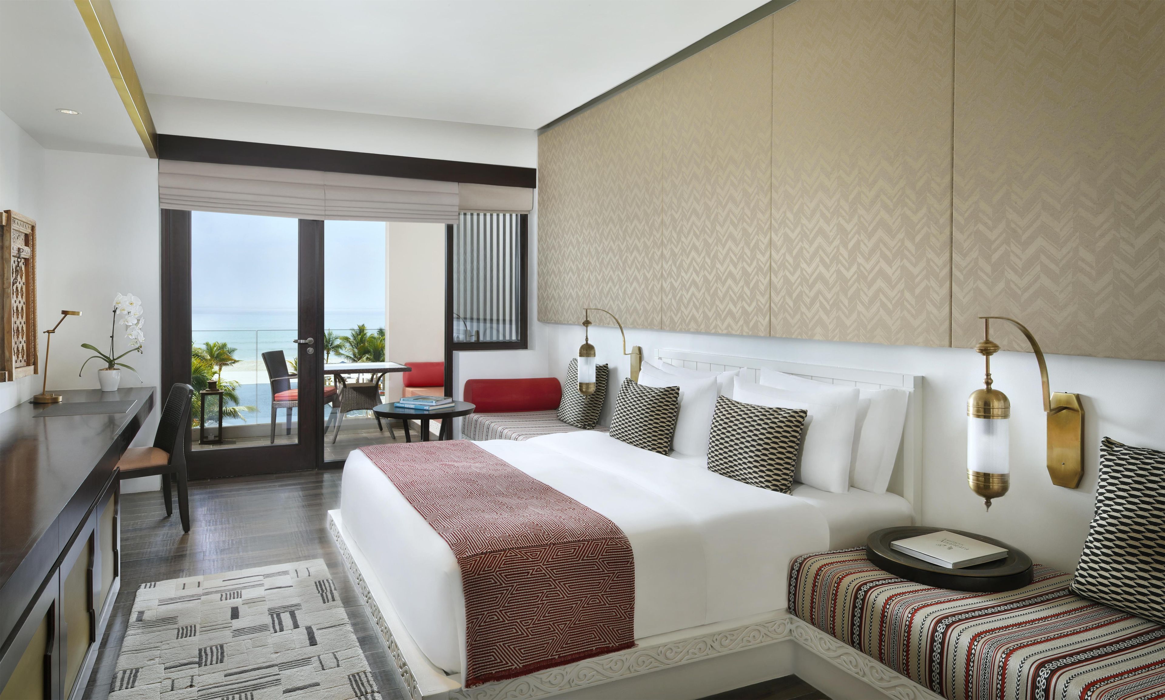 A hotel room with a large bed, a desk, a chair, a small table, and a view of the ocean.