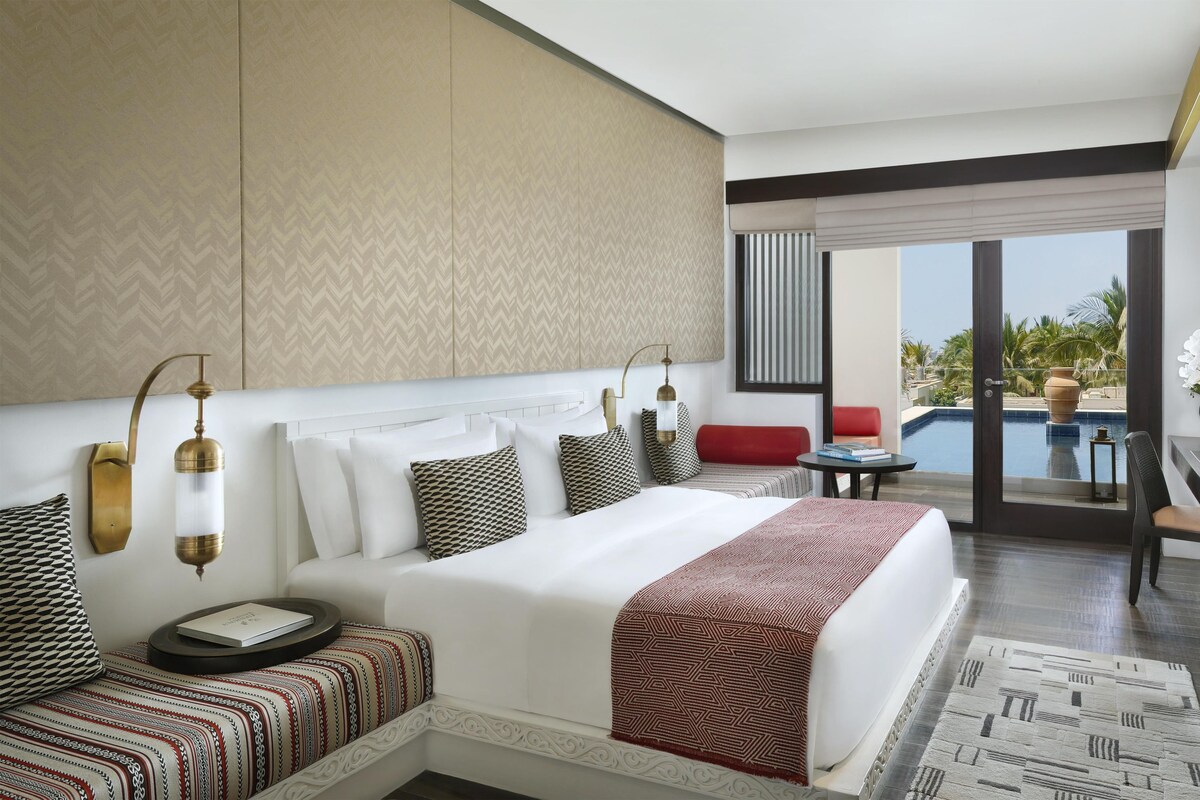 A hotel room with a bed, bedside table, and a view of a swimming pool.