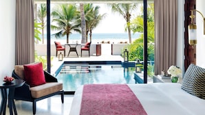Une chambre d’hôtel avec un grand lit, une petite table, une chaise et une vue sur l’océan grâce à de grandes fenêtres.
