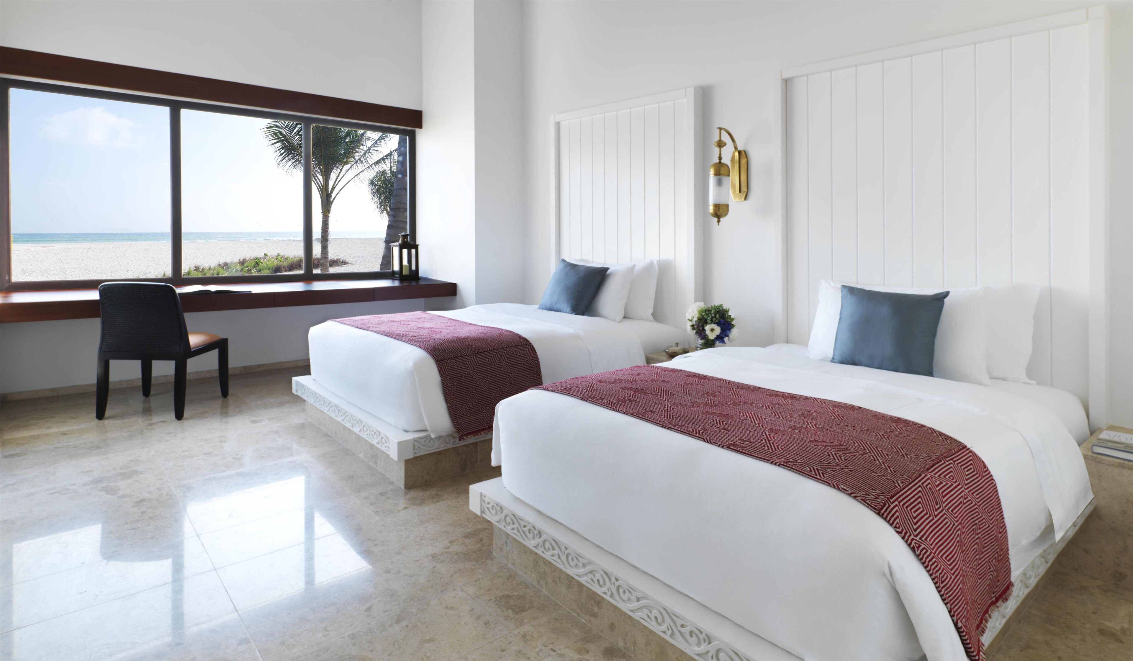 A hotel room with two beds, a view of the beach, and a chair by the window.