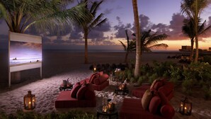 Un salon de plage avec des sièges rembourrés de couleur rouge, des palmiers et une vue sur le coucher de soleil.