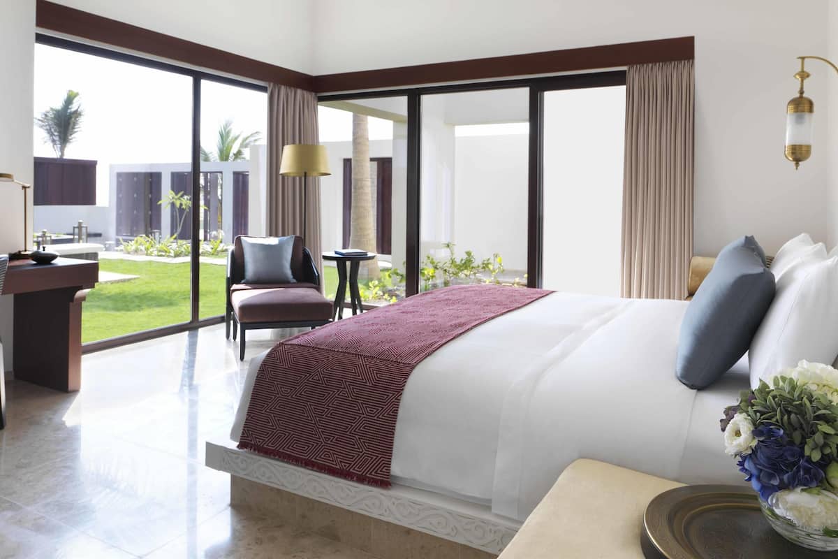 A hotel room with a large bed, a desk, a chair, a small table, and a view of the outdoors.