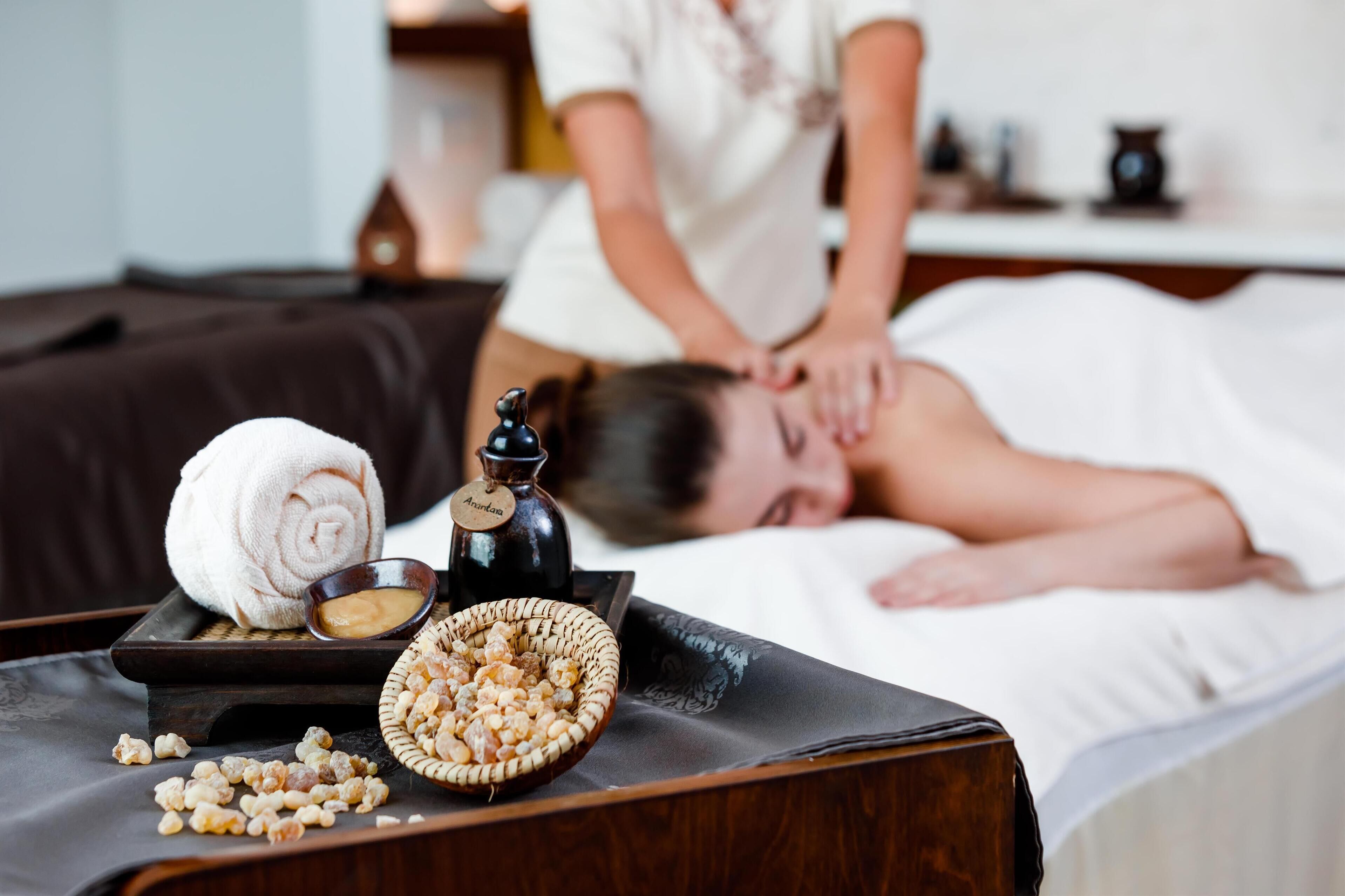 Une séance de massage avec une serviette, un bol de noix et une bouteille étiquetée « Arandana » sur une table en bois.
