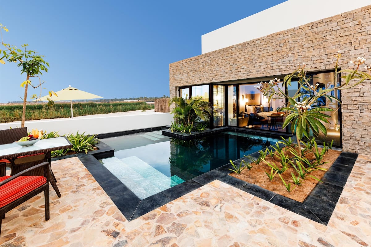A modern outdoor pool area with a stone-tiled deck, a dining table with chairs, and a lounge area with a sofa and coffee table.