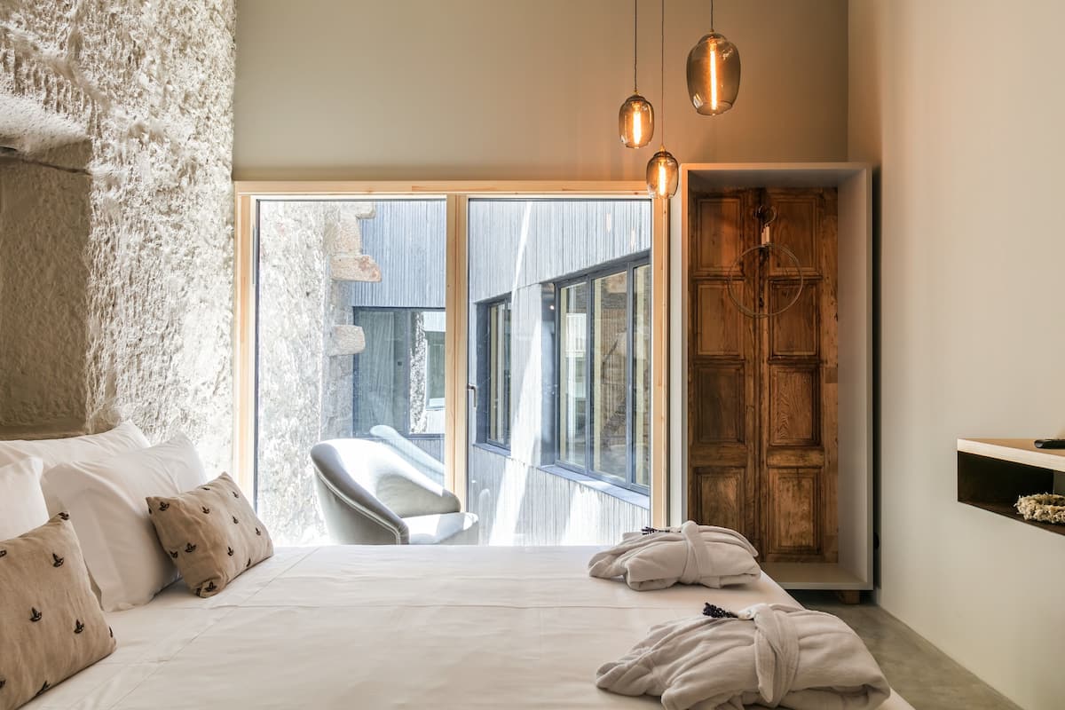 A bedroom with a large bed, a wooden wardrobe, and a view of the outside.