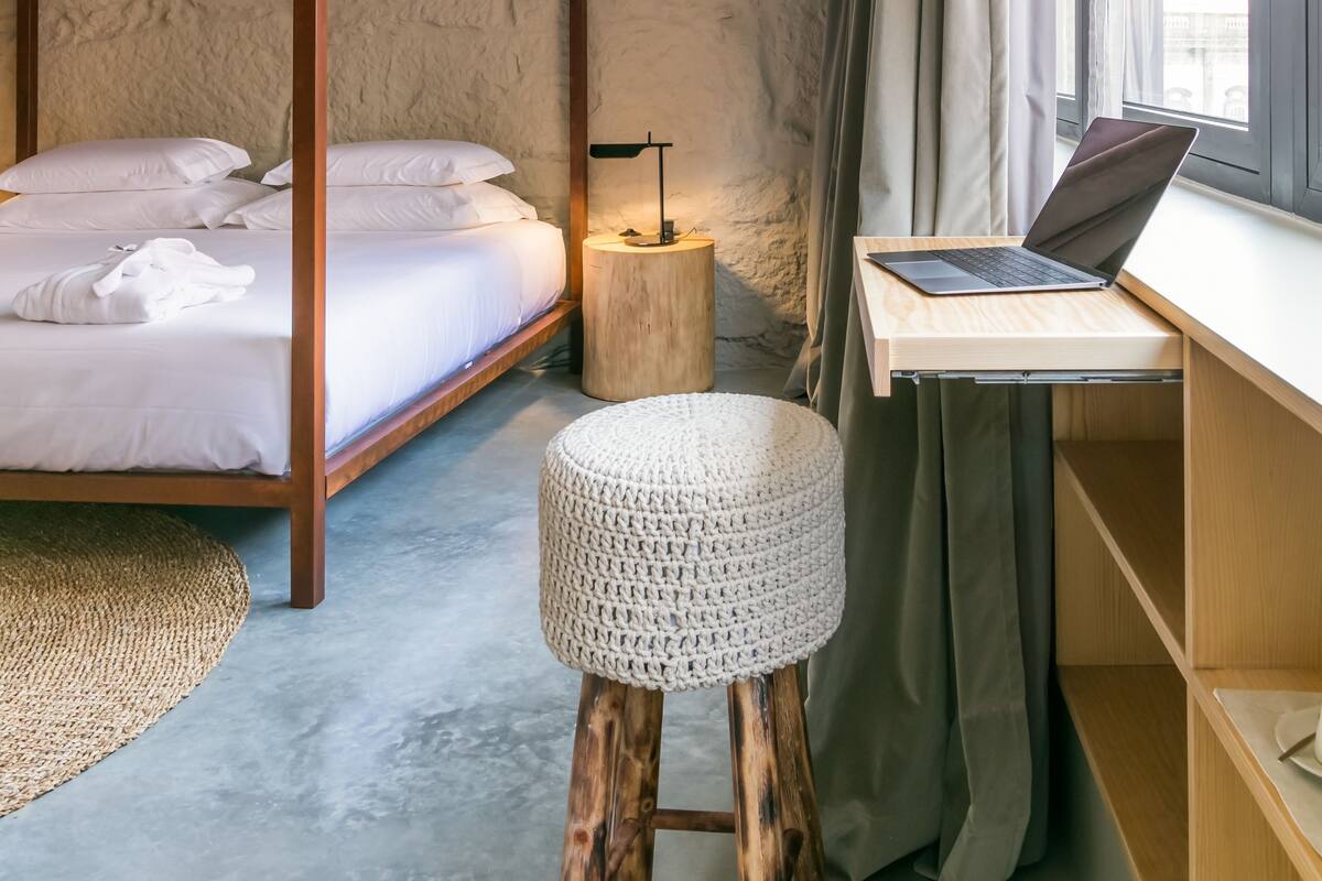A bedroom with a four-poster bed, a laptop on a desk, and a small round stool.