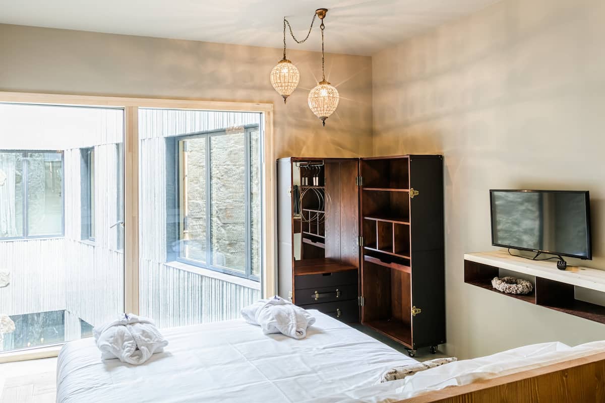 A bedroom with a bed, a wardrobe, a television, and a window with a view of trees.