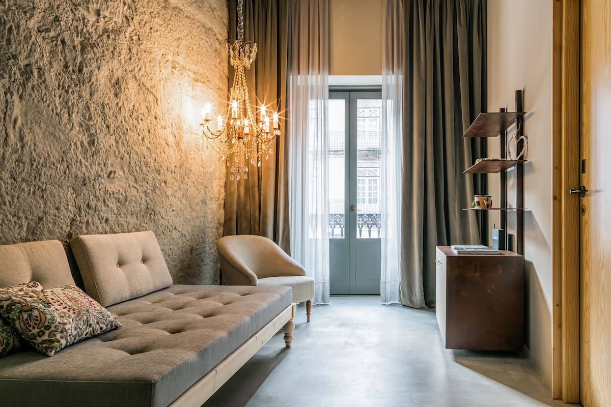 A modern living room with a stone wall, a sofa with patterned cushions, a chandelier, and a view through a glass door to an outdoor balcony.