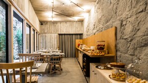 A modern dining area with wooden furniture, a stone wall, and a view of greenery. - Armazém Luxury Housing (Porto)