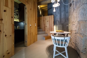 Un interior de madera con una mesa redonda y sillas blancas, una escalera y una pared de piedra.