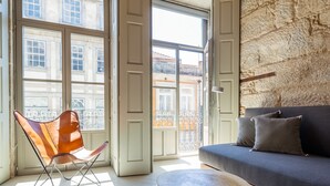 A room with a large window, a leather chair, a sofa, and a round wooden table. - Armazém Luxury Housing (Porto)