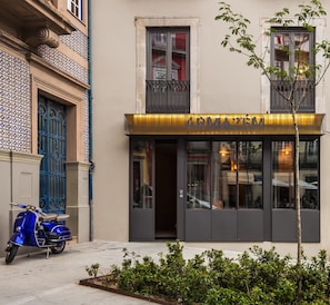 Un edificio con una moto azul estacionada frente a él, una entrada con portón y un letrero que dice "ARMACEM Luxury Housing".