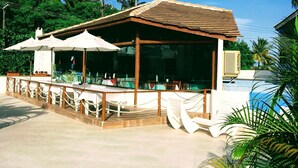 An outdoor seating area with tables and umbrellas, surrounded by palm trees and a clear blue sky. - Sueds Plaza (Porto Seguro)