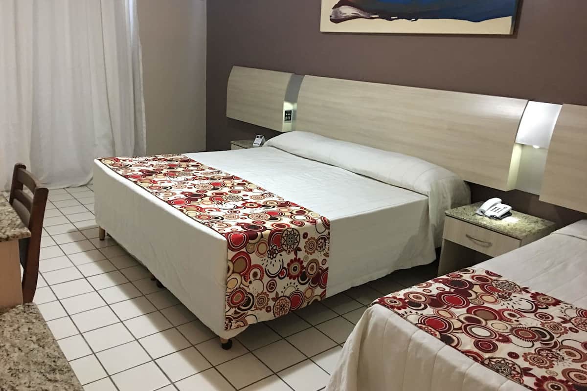 A hotel room with a bed, a bedside table with a phone, a chair, and a painting on the wall.