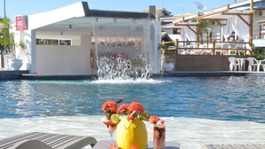 A pool area with a water feature, lounge chairs, and a table with a drink and fruit. - Sueds Plaza (Porto Seguro)