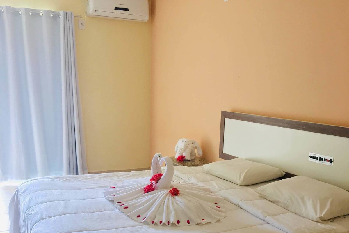 A hotel room with a bed, a headboard, a wall-mounted air conditioner, and a curtain.