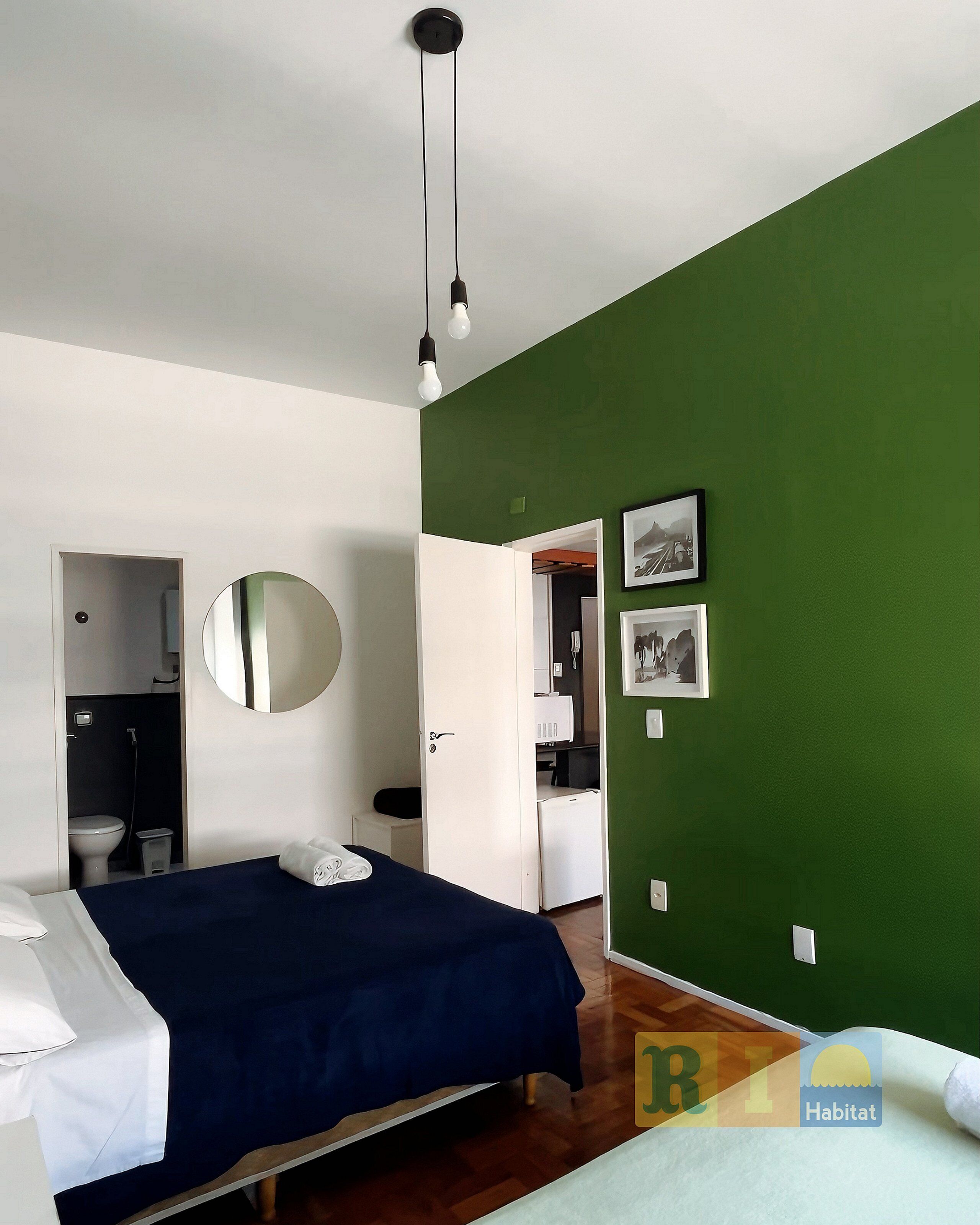 A bedroom with a bed, a mirror, a wardrobe, and a green wall.