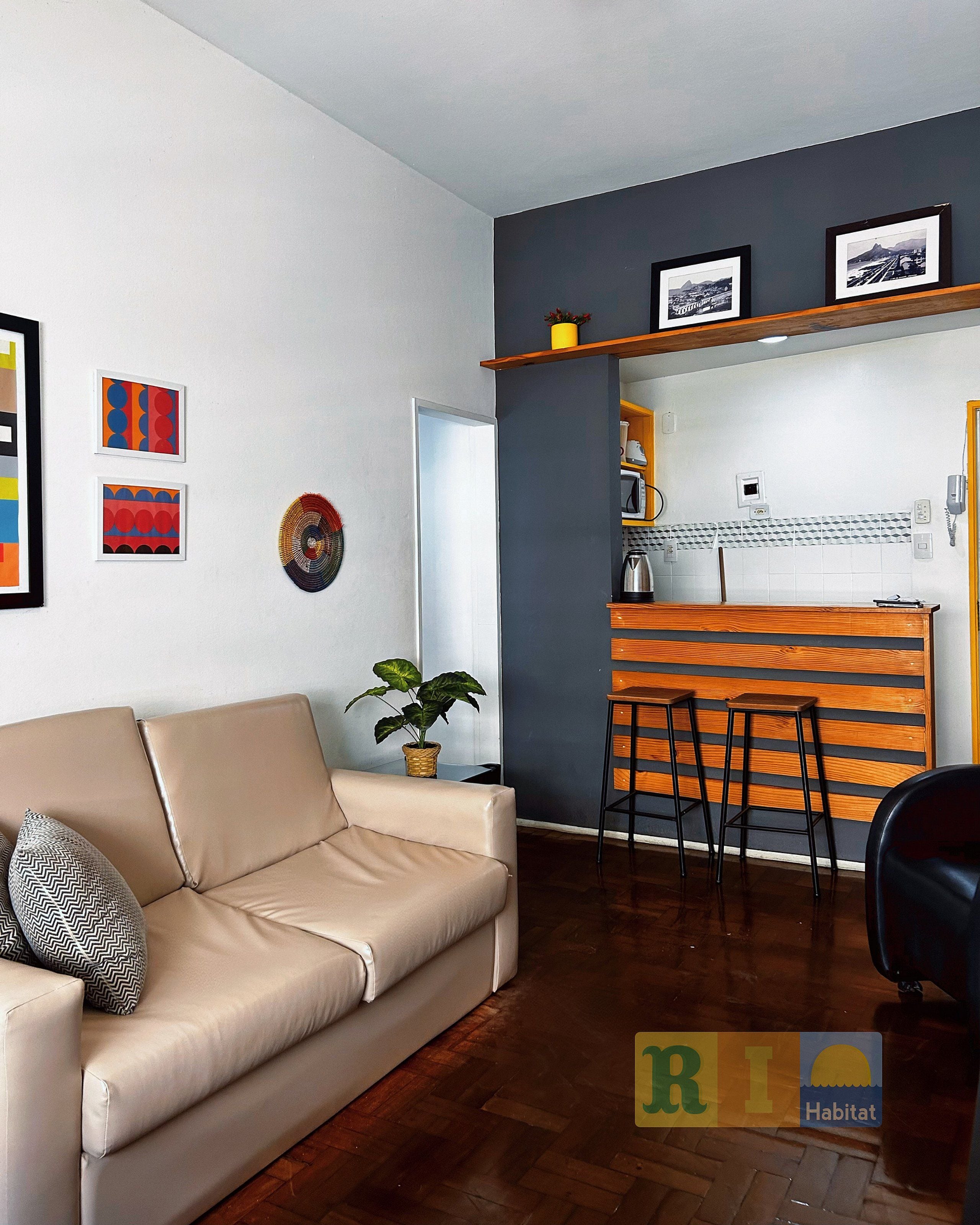 A modern living room with a beige sofa, a dining area with wooden chairs, and a kitchen with a microwave.