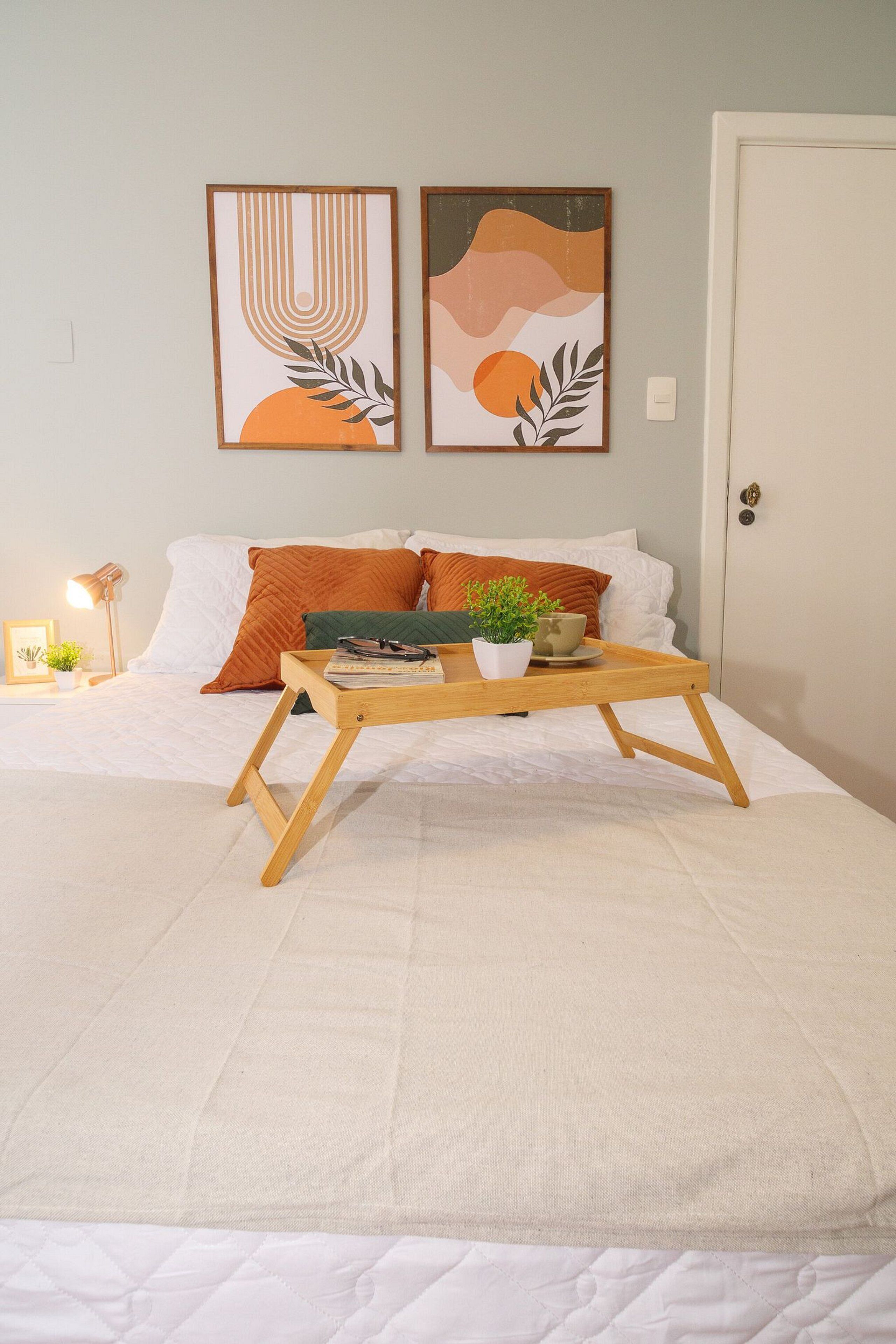 A neatly arranged bedroom with a bed, a bedside table with a lamp, and two framed artworks on the wall.