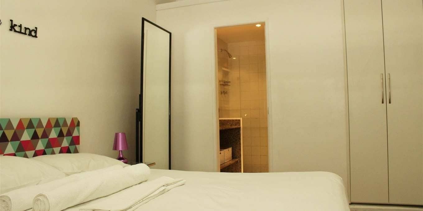 Habitació d'hotel amb un llit, un armari i un bany visible a través d'una porta oberta.