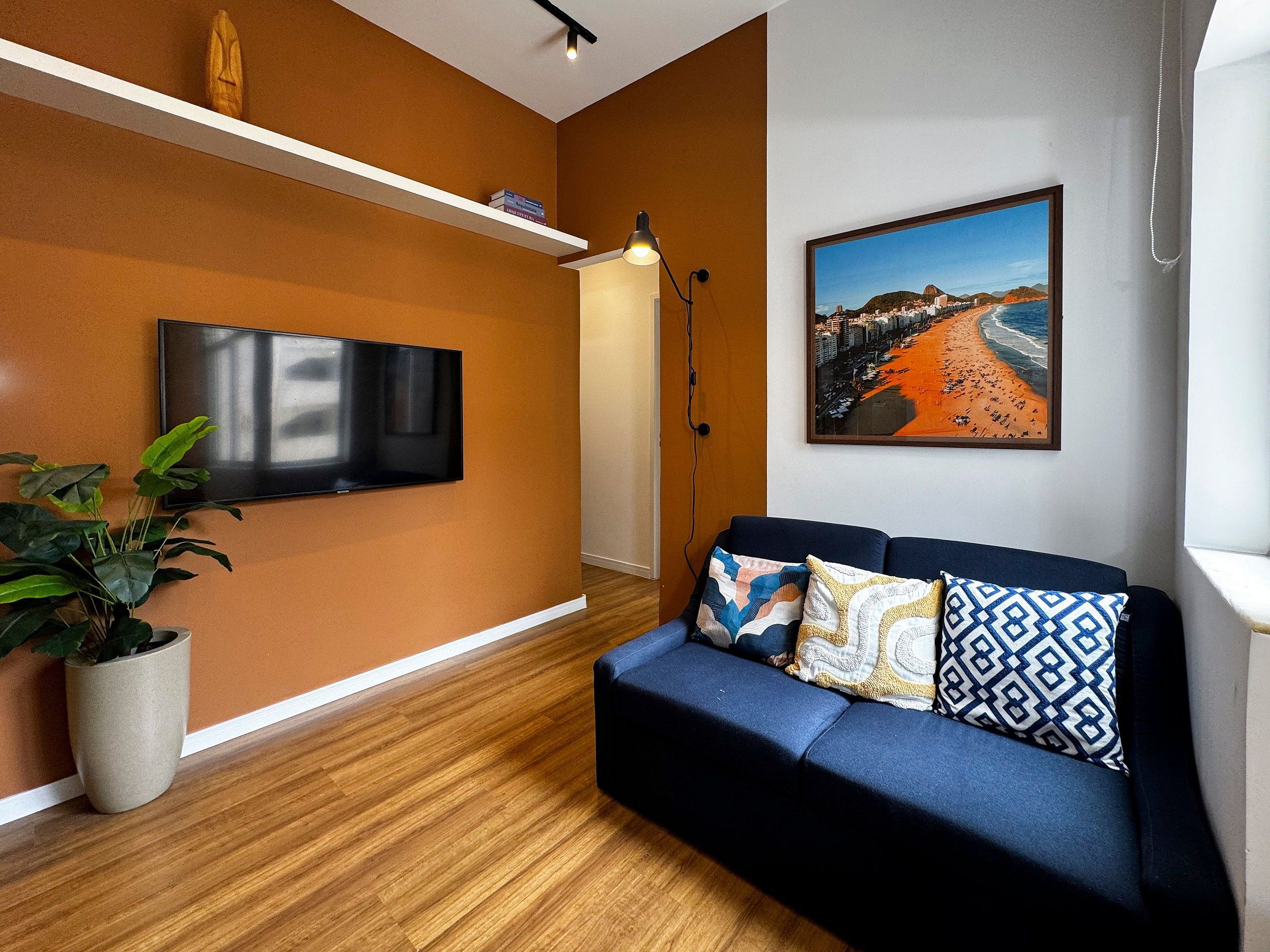 Una sala de estar moderna con un televisor de pantalla plana, un sofá con cojines estampados, una planta en maceta y un cuadro enmarcado de un paisaje urbano.