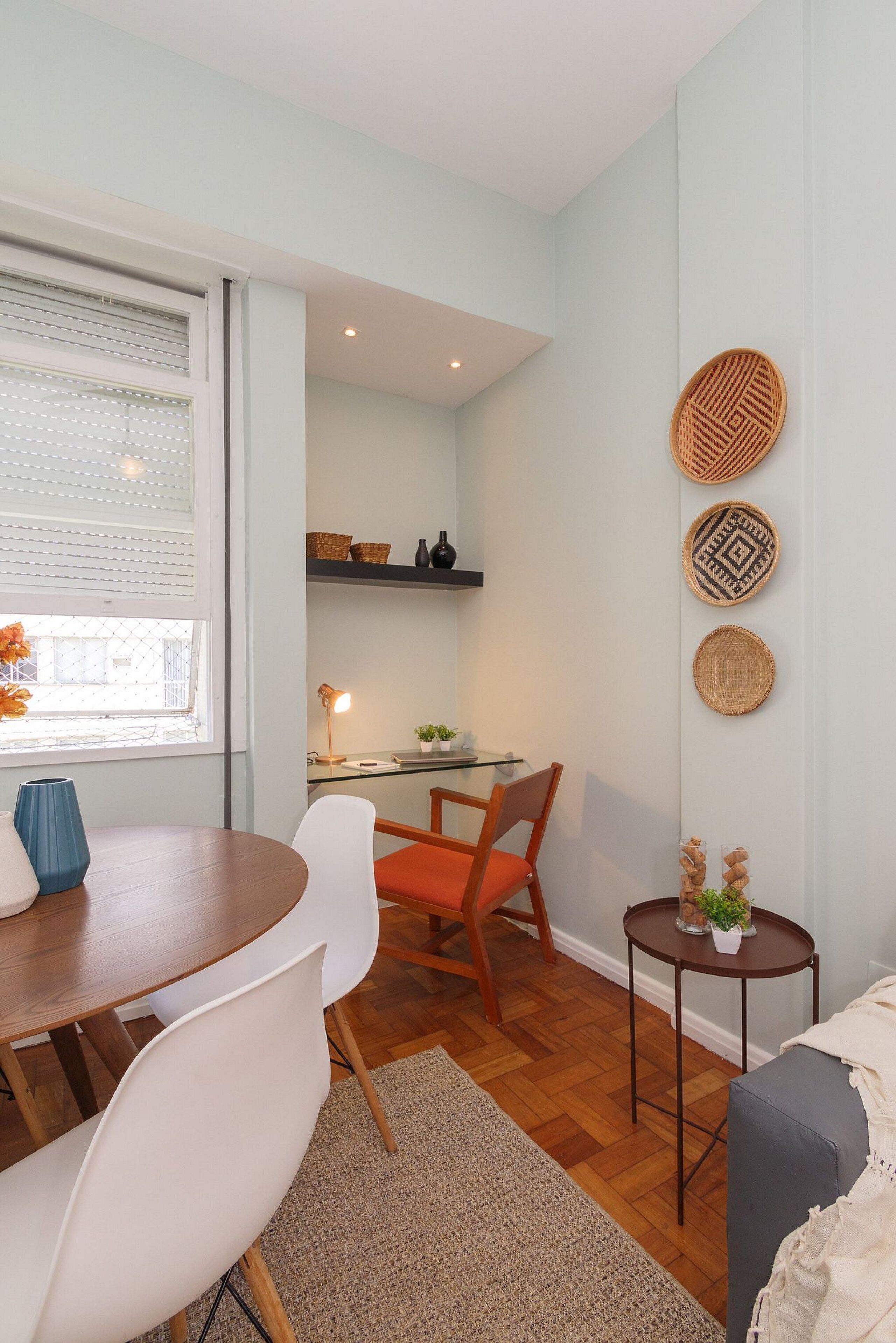 Una sala moderna con una mesa de comedor, sillas, un sofá, una mesita auxiliar con una planta, y una zona de cocina con un escritorio y estanterías.