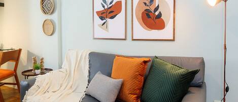Una sala moderna con un sofá gris, un reposapiés naranja y obras de arte en la pared.