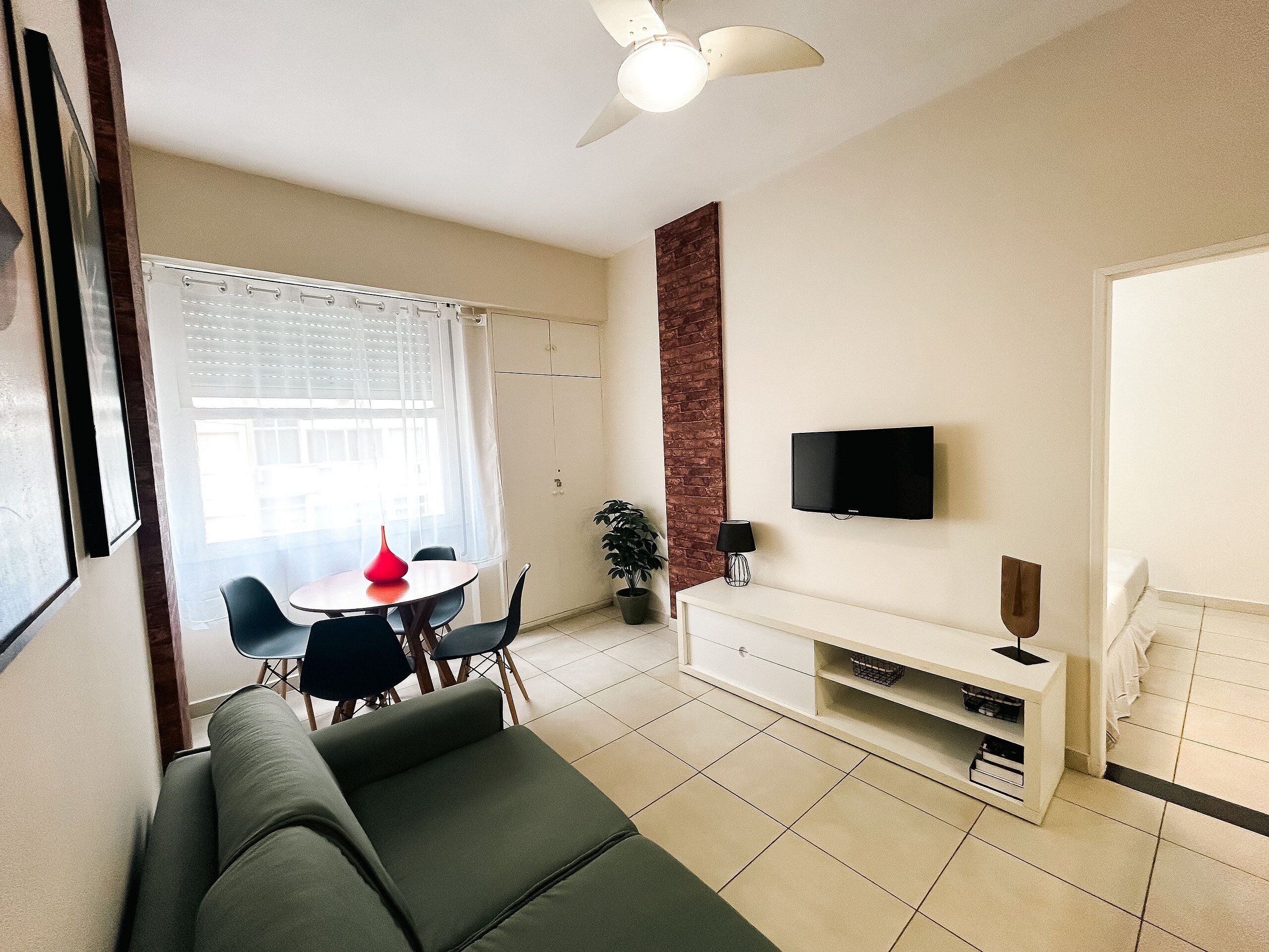 Een woonkamer met een bank, een eettafel met stoelen, een aan de muur bevestigde televisie en een plafondventilator.