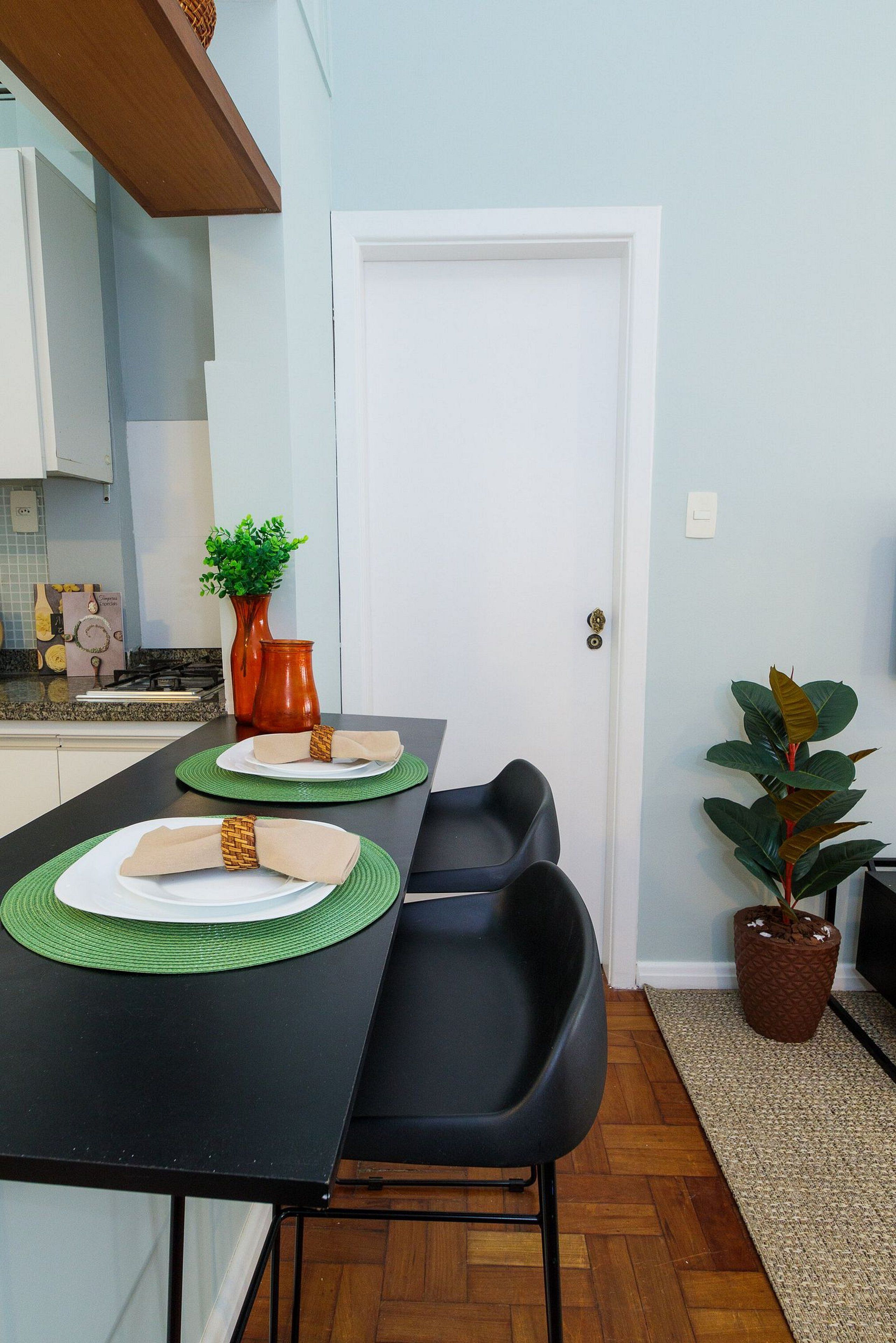 A dining area with a black table, two chairs, a white door, a potted plant, and a vase with greenery.
