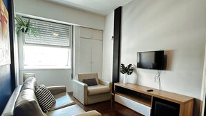 Een woonkamer met een bank, fauteuil, televisie en plafondventilator.