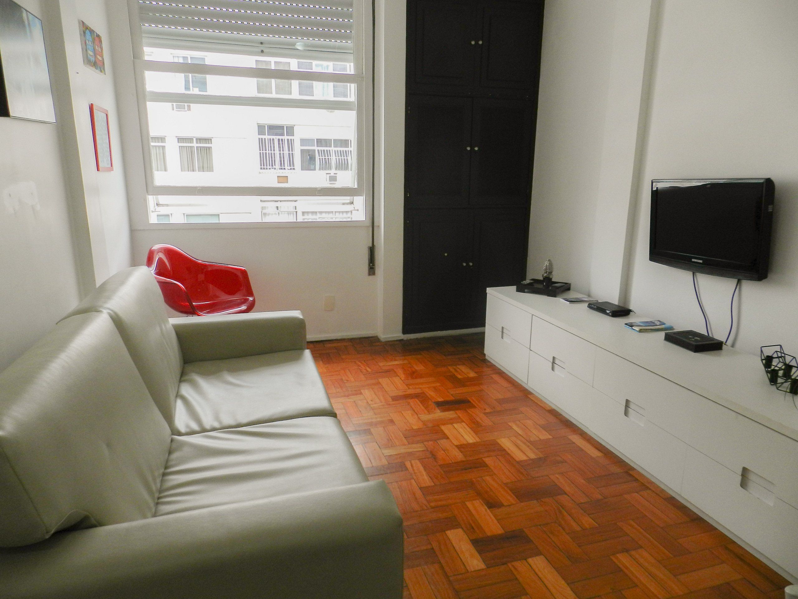 Una sala de estar con un sofá, un televisor montado en la pared, piso de madera en espiga y una puerta.