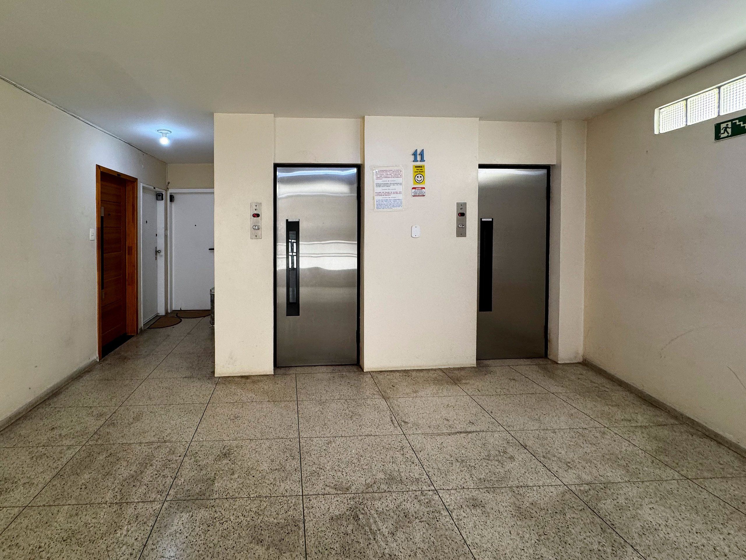 A hallway with three doors, a wooden door on the left, and two elevator doors.