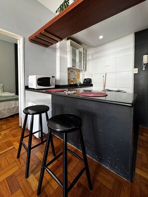 A compact kitchen with a black countertop, two stools, a microwave, and a cabinet. - Rio Habitat Almirante (Rio de Janeiro)