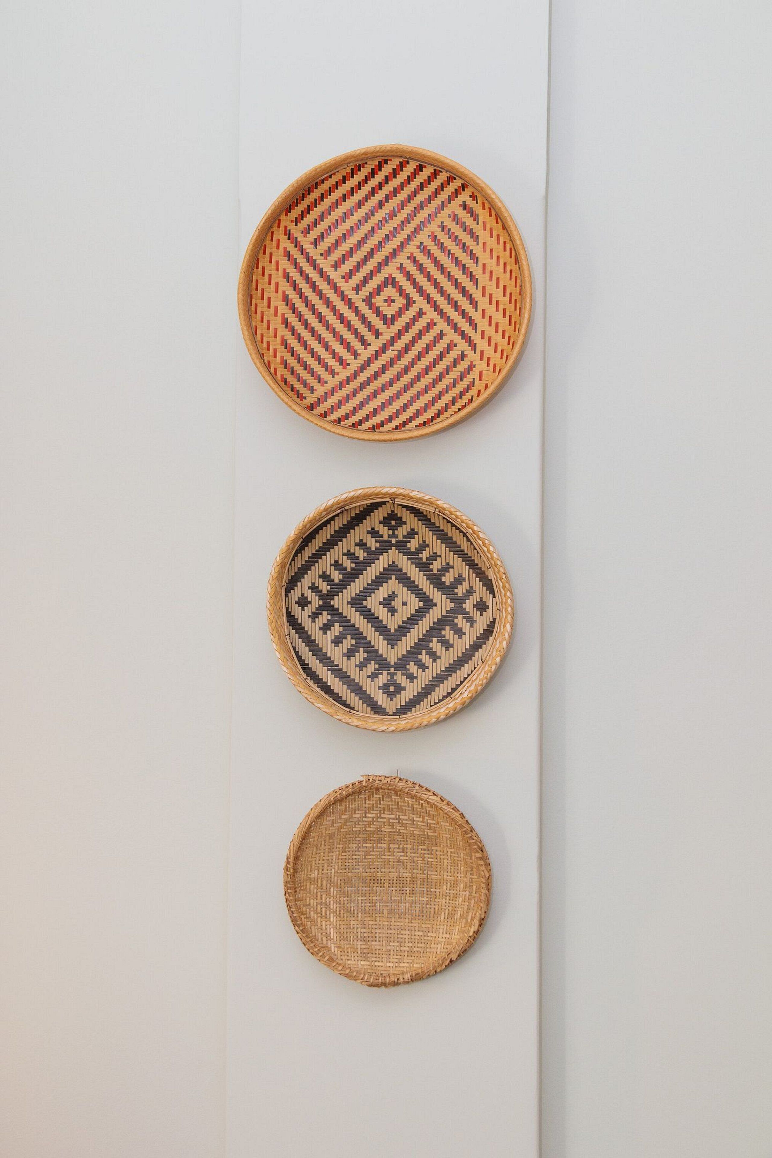 Three woven baskets of different sizes and patterns arranged vertically on a plain wall.