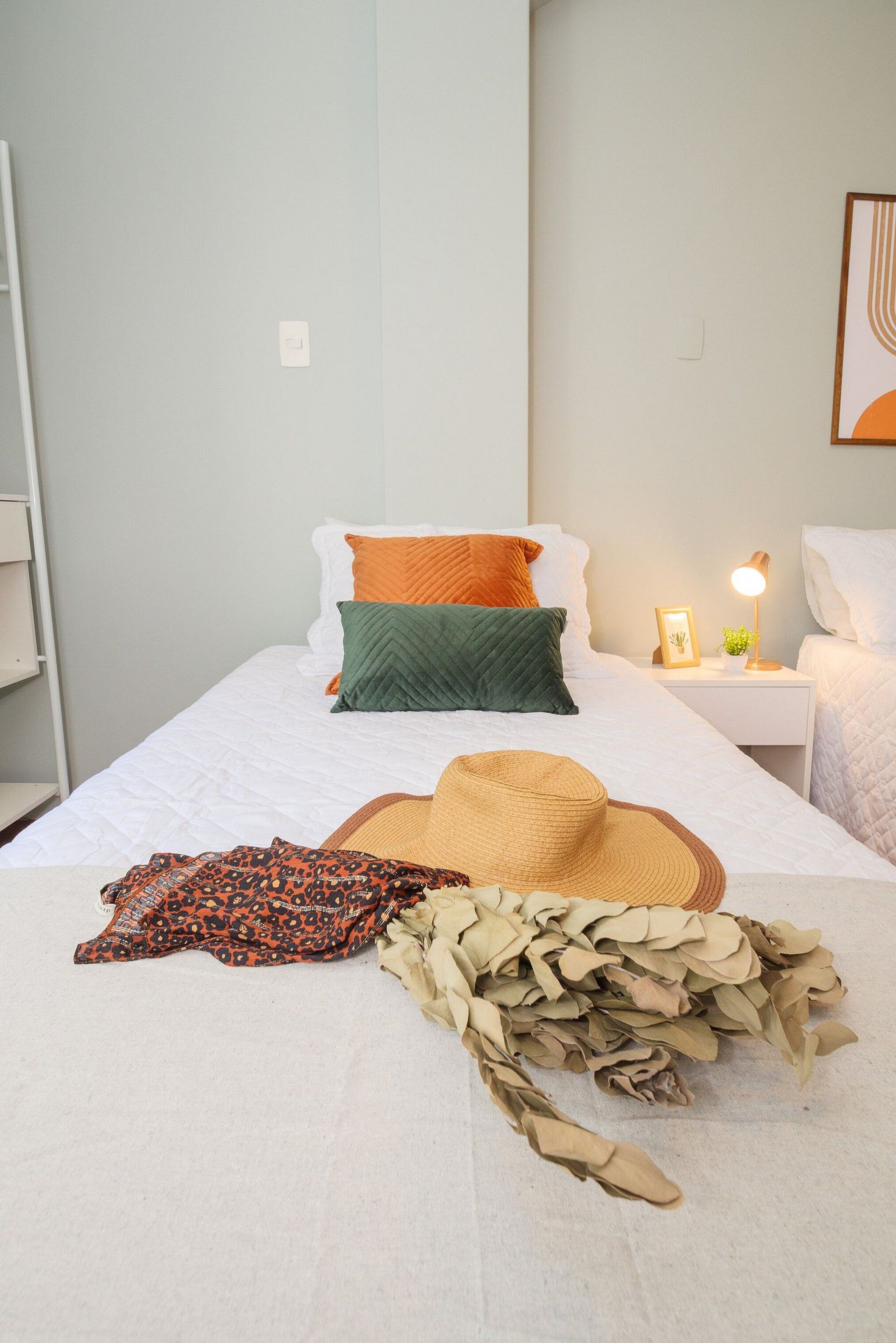 Una cama bien hecha con almohadas, una lámpara de noche y un sombrero sobre la cama.