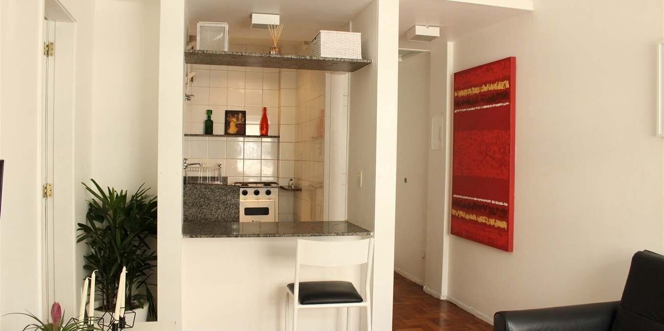 Una cucina con mobili bianchi, un piano di lavoro in granito, un fornello e un'opera d'arte rossa appesa al muro.