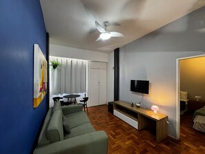Un salon comprenant un canapé, un téléviseur, un ventilateur de plafond et un coin repas avec une table et des chaises.