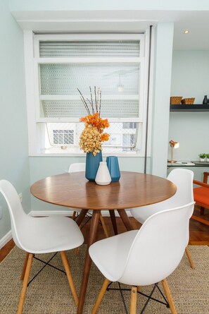 Un comedor con una mesa redonda de madera, sillas blancas y un florero con flores.