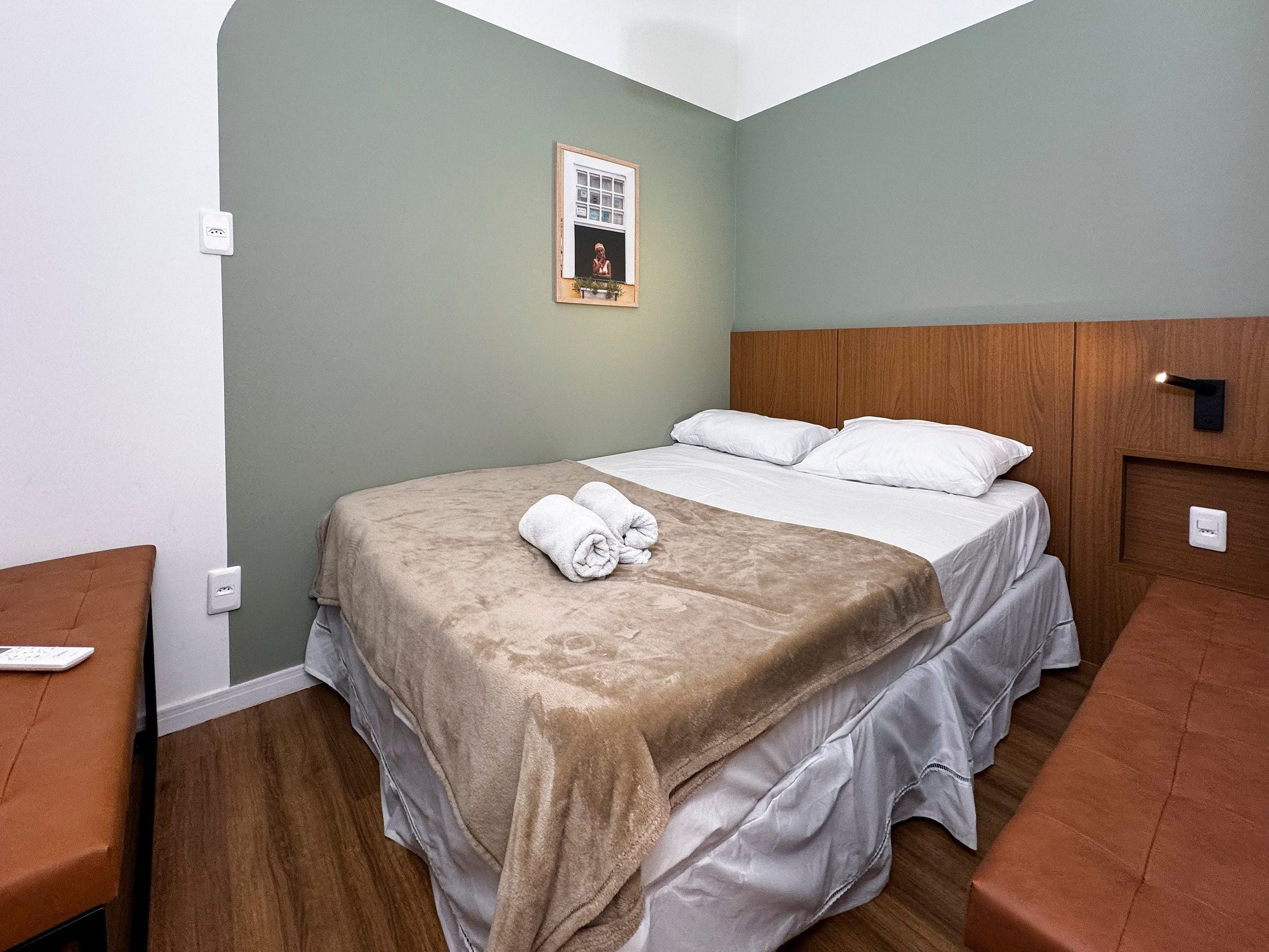 Une chambre d’hôtel avec un lit, une table de chevet et un luminaire fixé au mur.