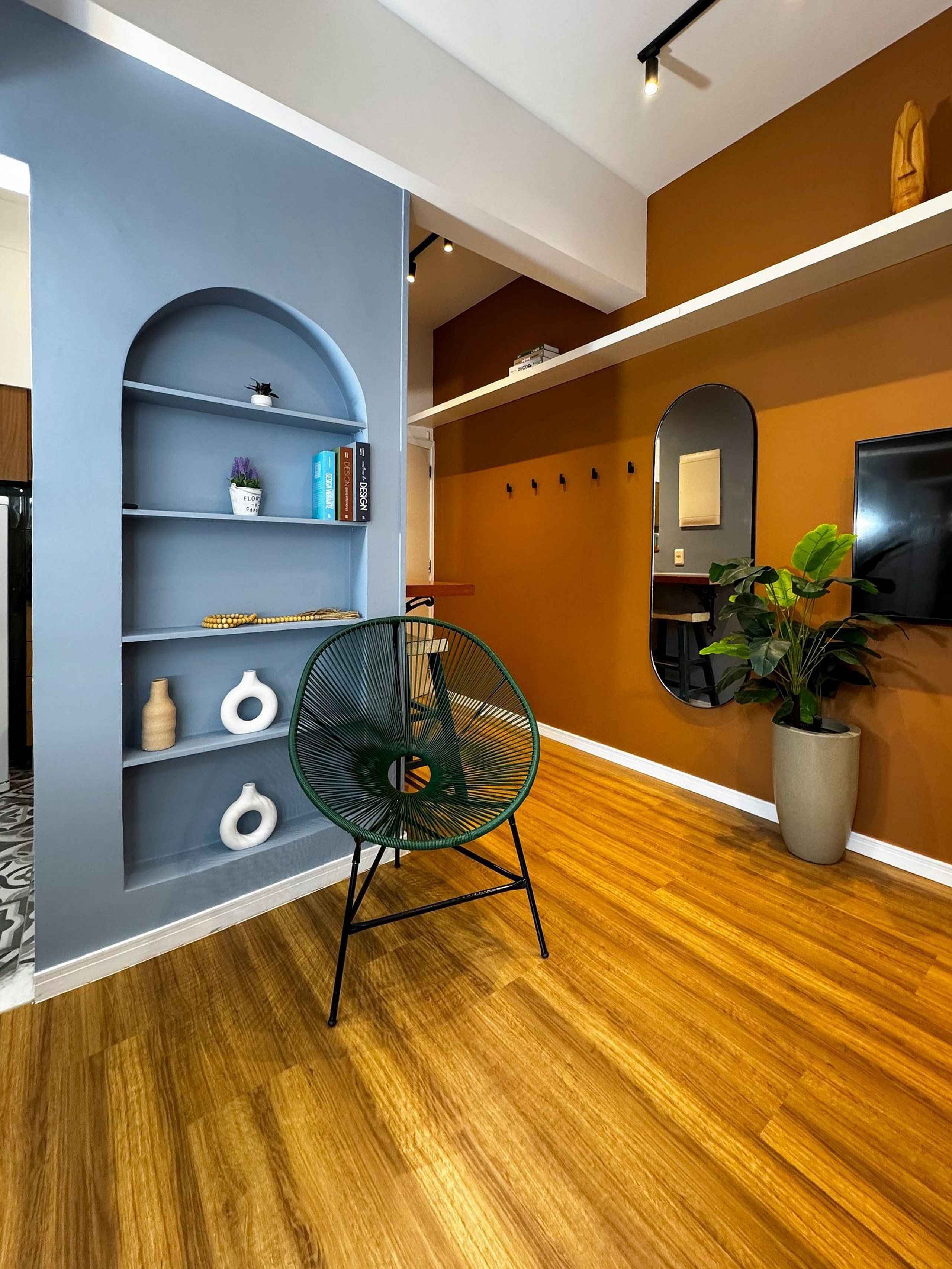 Um interior moderno com piso de madeira, uma cadeira verde, uma estante de livros e um vaso com planta.