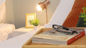 A neatly made bed with a white comforter, a bedside table with a lamp, a framed picture, and a small plant. - Rio Habitat Almirante (Rio de Janeiro)