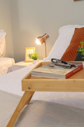 A neatly made bed with a white comforter, a bedside table with a lamp, a framed picture, and a small plant. - Rio Habitat Almirante (Rio de Janeiro)