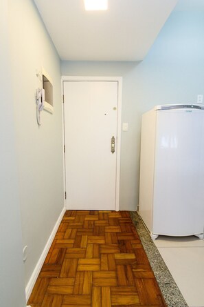 A hallway with a wooden floor, a white door, and a white refrigerator. - Rio Habitat Almirante (Rio de Janeiro)