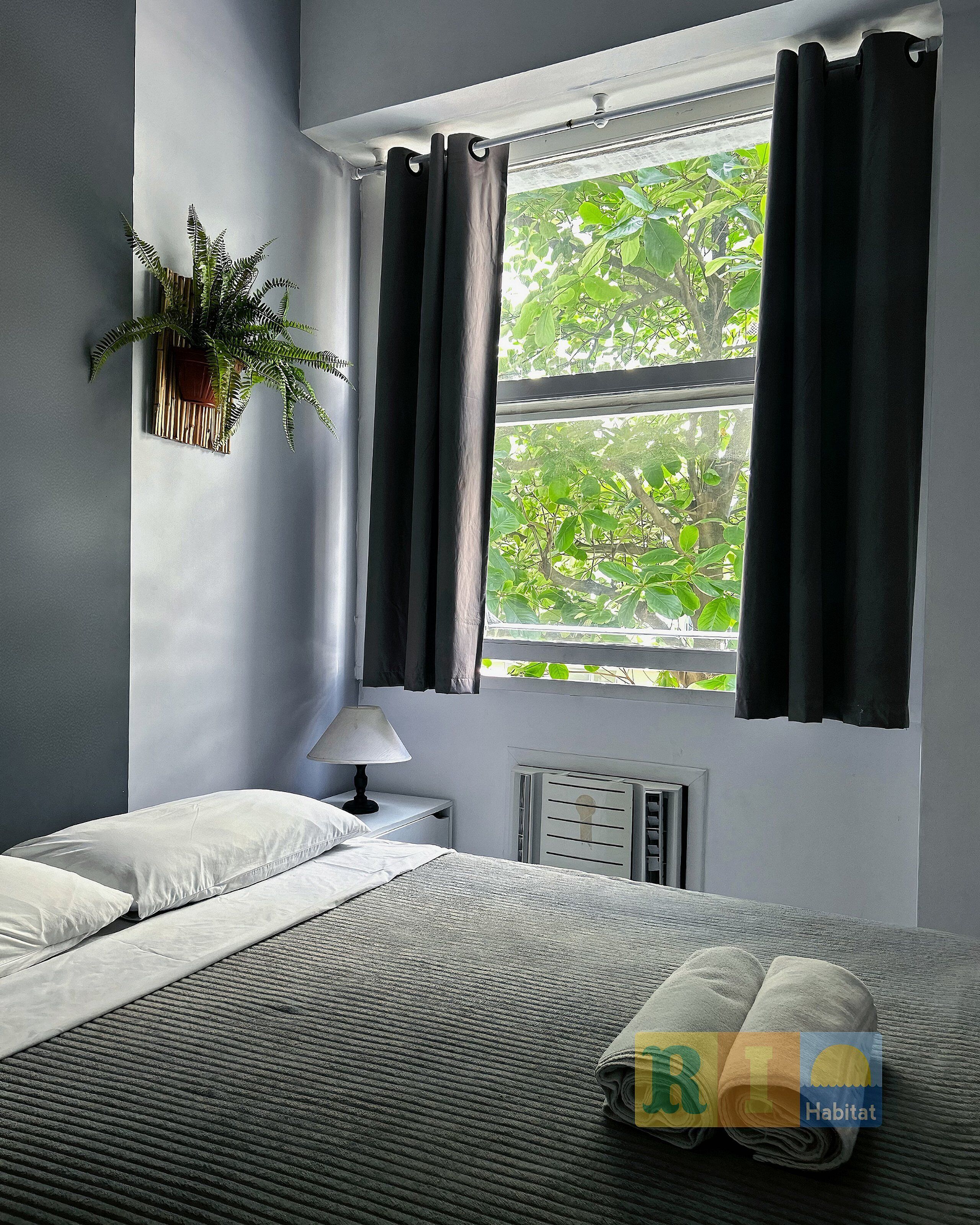 A bedroom with a bed, a bedside table with a lamp, a radiator, and a window with curtains.