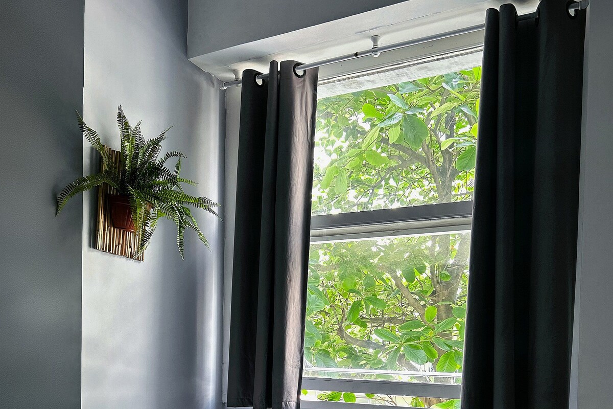 Une chambre à coucher avec un lit, une table de chevet avec une lampe, un radiateur et une fenêtre avec des rideaux.